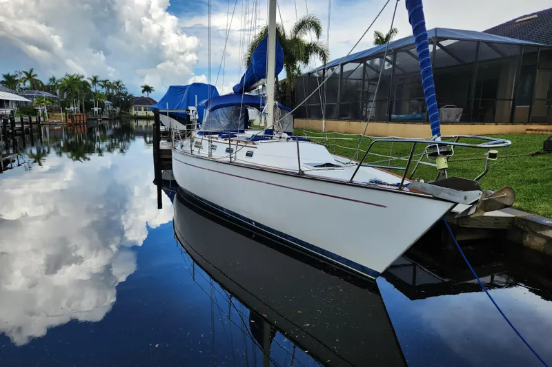 The Image of 1990 Catalina/Morgan 44 Center Cockpit sailboat docked on a calm, reflective waterway. - 0