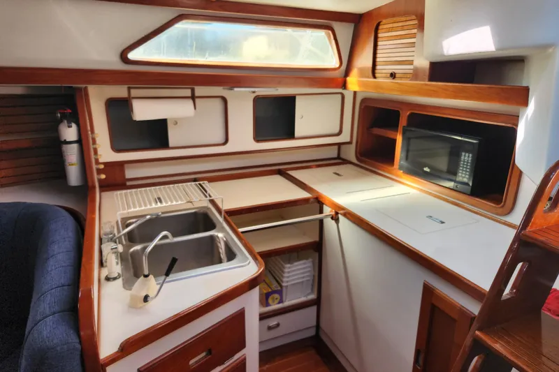 Slide: The Image of 1990 Morgan 44 Center Cockpit yacht kitchen with sink, microwave, and wooden cabinetry. - 22