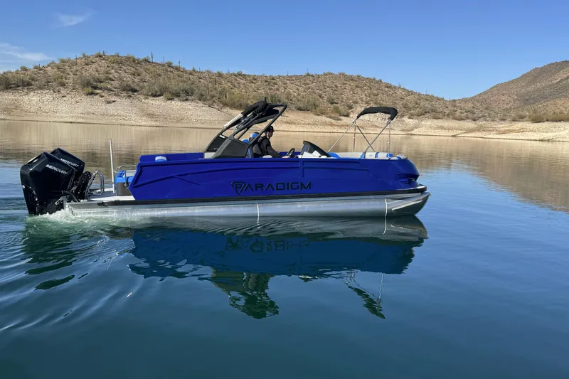 Slide: The Image of 2025 Paradigm 27SST pontoon boat on a calm lake with desert landscape. - 2
