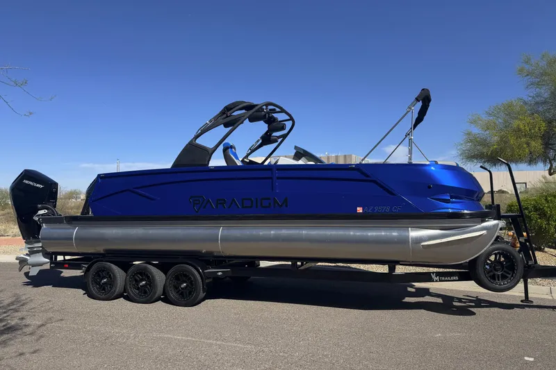 Slide: The Image of 2025 Paradigm 27SST pontoon boat on trailer, blue exterior, parked outdoors. - 7