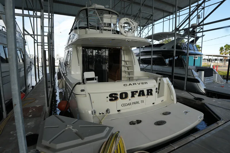 Slide: The Image of 2004 Carver 560 Voyager yacht docked in marina, rear view with "So Far" name. - 2