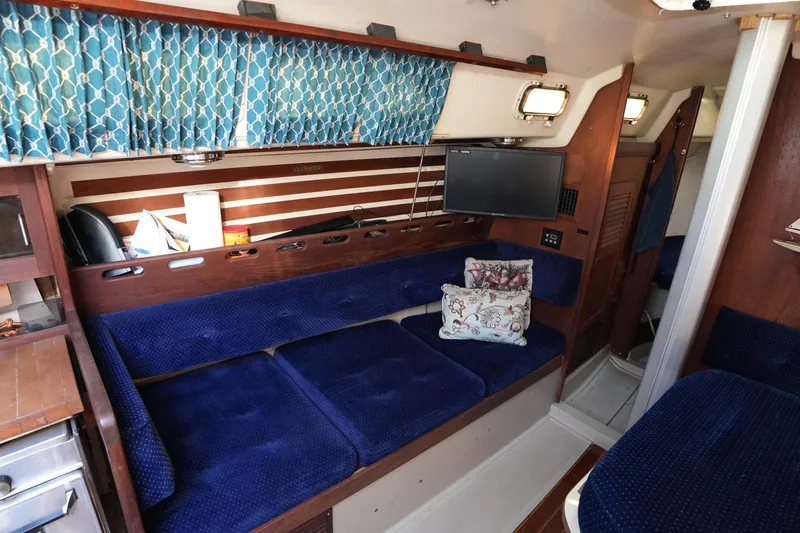 Slide: The Image of 1984 O'Day 30 sailboat interior with blue seating, floral pillows, and a mounted TV. - 13