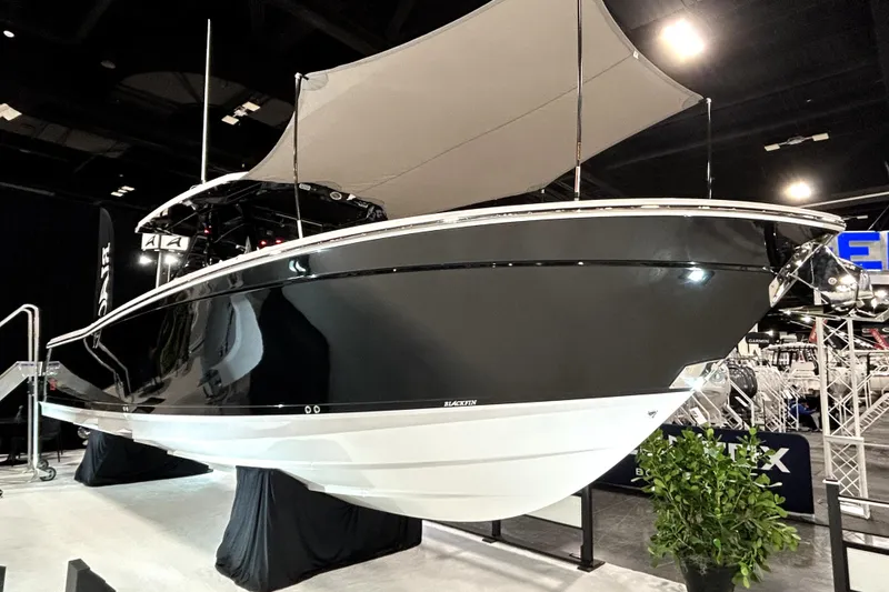 Slide: The Image of 2026 Blackfin 332 CC boat displayed indoors with canopy and sleek black design. - 0