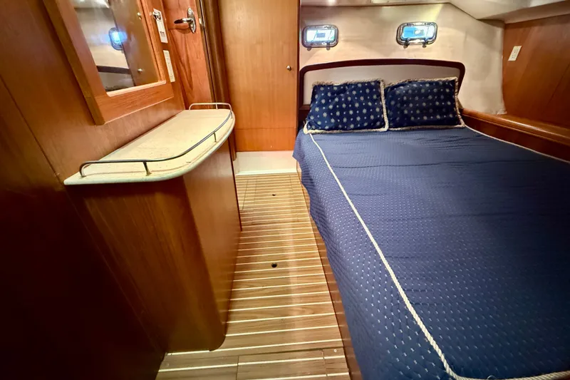 Slide: The Image of Interior of 2003 Hunter 426 Deck Salon with blue bedding and wooden accents. - 14