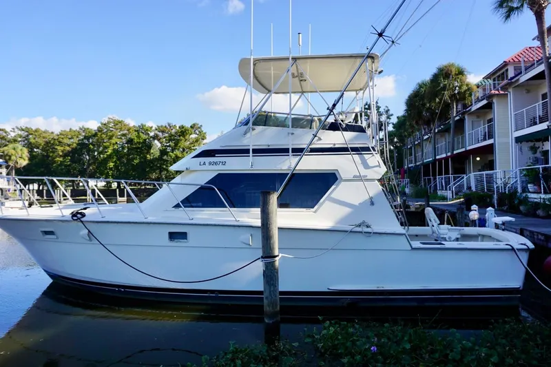 Slide: The Image of 1986 Hatteras 41 Convertible yacht docked by waterfront homes, under a clear blue sky. - 1