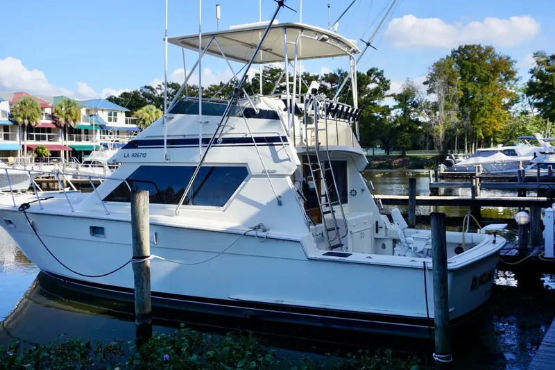 Slide: The Image of 1986 Hatteras 41 Convertible yacht docked at a marina, surrounded by trees and colorful buildings. - 2