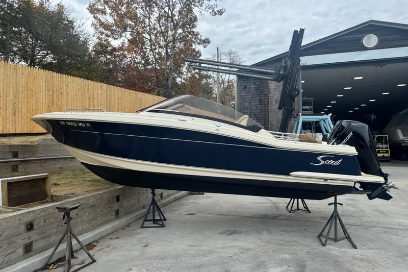 The Image of 2024 Scout 215 Dorado boat on stands, outdoors near a wooden fence and building. - 1