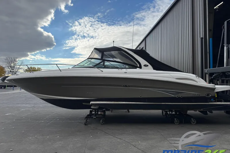 The Image of 2005 Sea Ray 290 Sun Sport boat on trailer, parked outside a warehouse under a cloudy sky. - 0