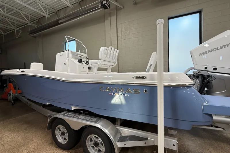 Slide: The Image of 2026 Caymas 24 HB boat in showroom, featuring sleek blue design and Mercury engine. - 3