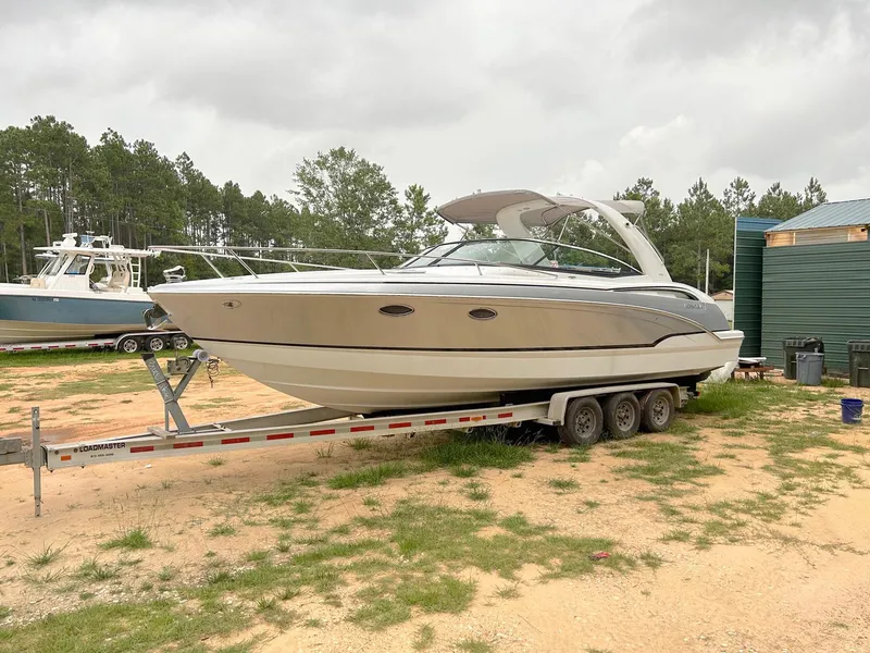 The Image of 2008 Formula 310 Sun Sport boat on trailer, parked outdoors, surrounded by trees and other boats. - 0