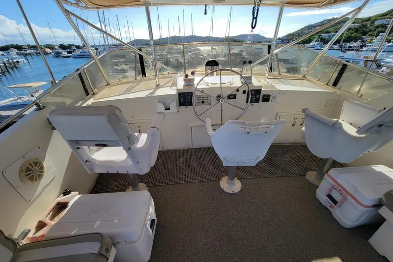 Slide: The Image of 1982 Hatteras 56 Wide Body yacht helm with three seats, overlooking marina and hills. - 21