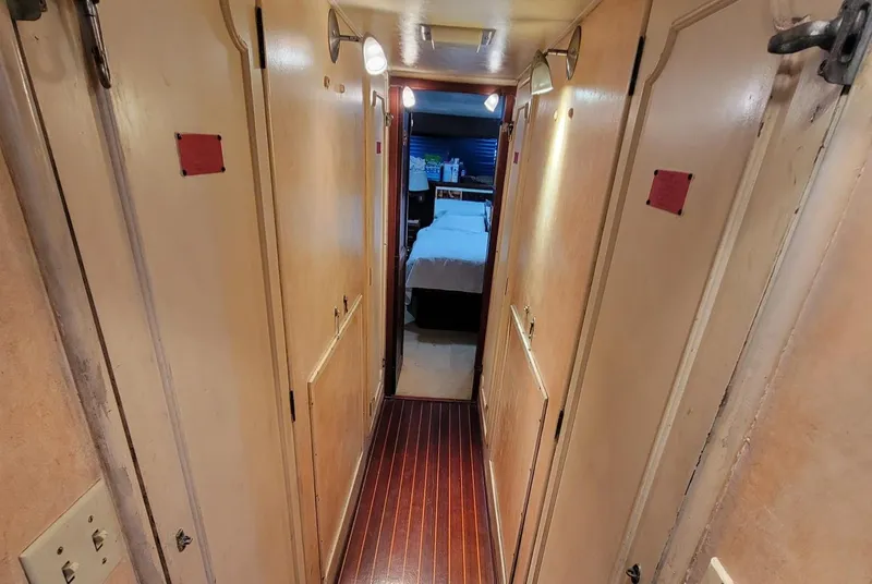 Slide: The Image of Narrow hallway inside 1982 Hatteras 56 Wide Body yacht, featuring wooden flooring and cabin doors. - 32