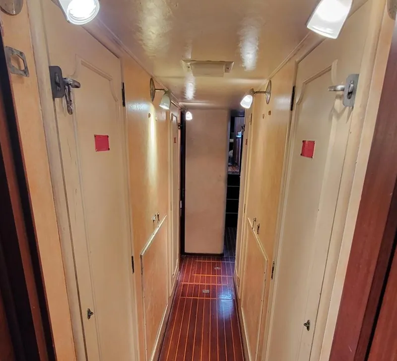 Slide: The Image of Narrow hallway inside 1982 Hatteras 56 Wide Body yacht with wooden flooring and multiple doors. - 38