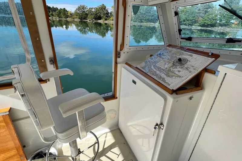 Slide: The Image of 1988 Jarvis Newman Hardtop Cruiser interior with chair, navigation map, and scenic water view. - 2