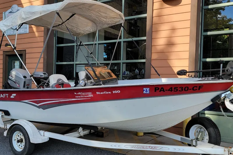 Slide: The Image of 1999 Starcraft Starfire 160 SC boat with canopy on trailer, parked outside a building. - 1