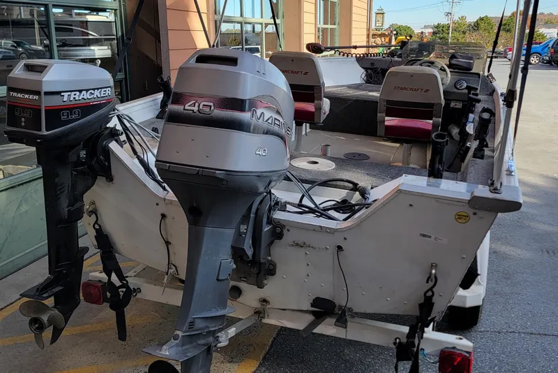 Slide: The Image of 1999 Starcraft Starfire 160 SC boat with dual outboard motors, parked outside a building. - 3