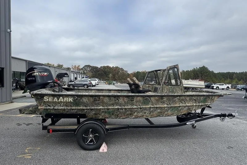The Image of 2026 SeaArk 1872 MVJT camo boat on trailer, parked outdoors near buildings. - 0