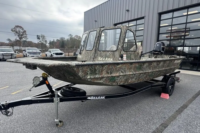 Slide: The Image of 2026 SeaArk 1872 MVJT camo boat on trailer, parked outside a building. - 4
