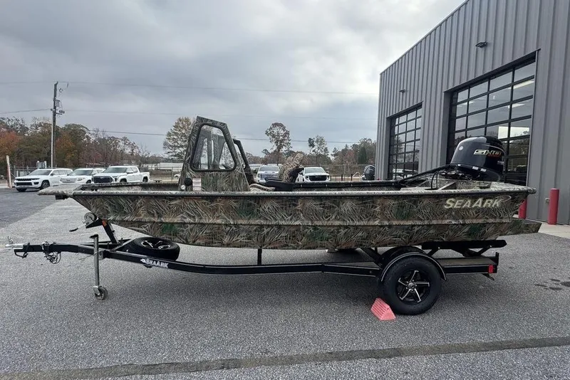 Slide: The Image of 2026 SeaArk 1872 MVJT camo boat on trailer, parked outside a building. - 5