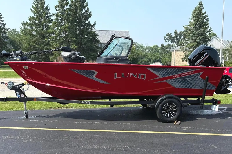 The Image of 2025 Lund 1675 Adventure Sport boat on trailer, vibrant red, parked outdoors. - 0