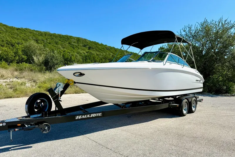 Slide: The Image of 2010 Cobalt 232 boat on trailer, parked outdoors with lush green background. - 10