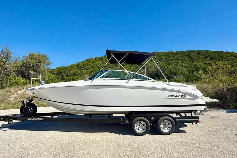 Slide: The Image of 2010 Cobalt 232 boat on trailer, parked outdoors under clear blue sky. - 13