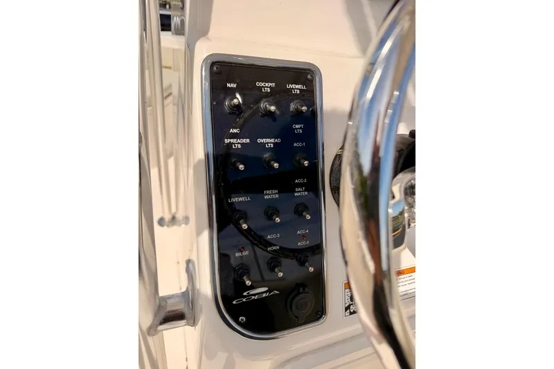 Slide: The Image of 2023 Cobia 220 Center Console boat control panel with various switches and steering wheel. - 19