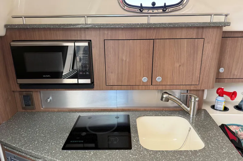 Slide: The Image of 2019 Boston Whaler 315 Conquest kitchen with microwave, stove, sink, and wooden cabinets. - 17
