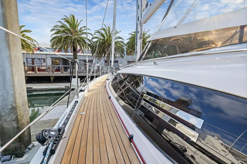 Slide: The Image of 2020 Hylas H57 yacht docked, showcasing sleek design and wooden deck with palm trees in background. - 54