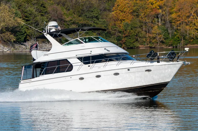 Slide: The Image of 2000 Carver 450 Voyager Pilothouse cruising on a serene lake with autumn foliage. - 1