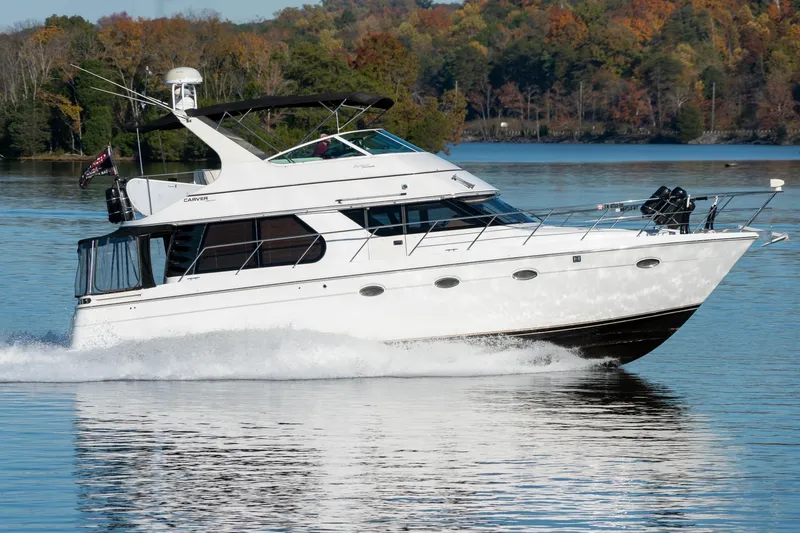 Slide: The Image of 2000 Carver 450 Voyager Pilothouse cruising on a serene lake with autumn foliage. - 2