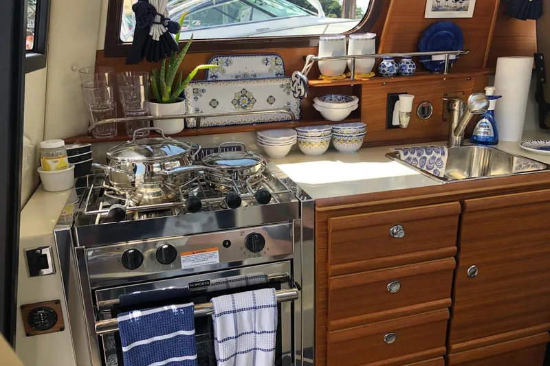 Slide: The Image of 2023 Ranger Tugs R-27 kitchen with stove, sink, and wooden cabinetry. - 19