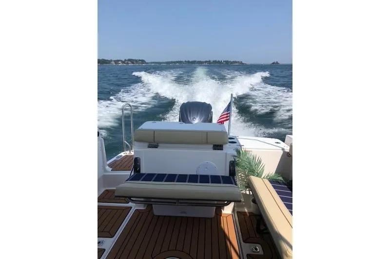 Slide: The Image of 2023 Ranger Tugs R-27 cruising on open water, rear view with American flag. - 9