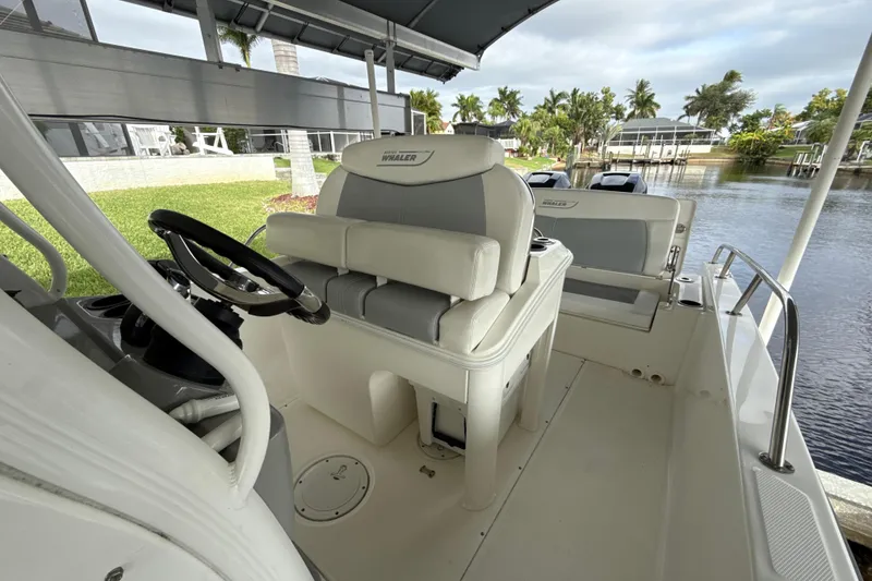 Slide: The Image of 2015 Boston Whaler 270 Dauntless boat interior with helm and seating, docked by water. - 11