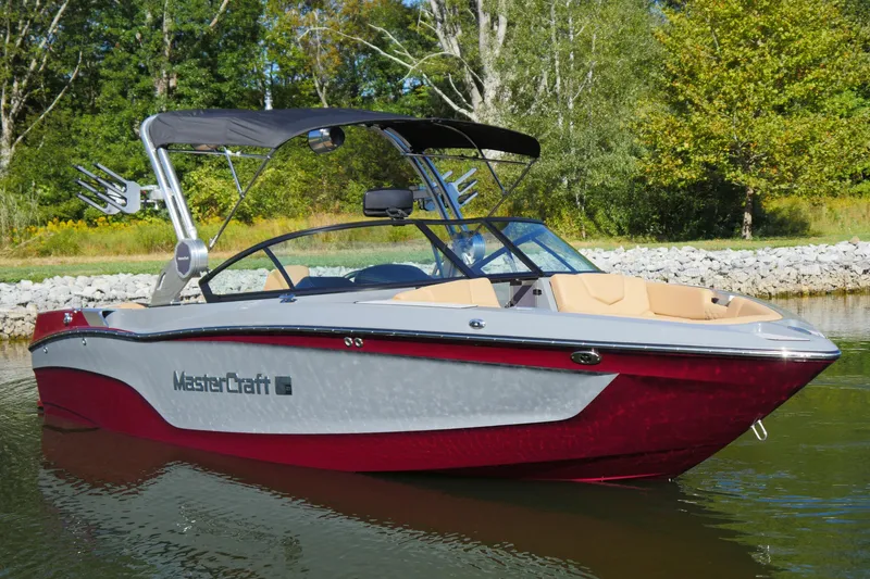 The Image of 2022 MasterCraft XT23 boat on a calm lake with lush green background. - 1