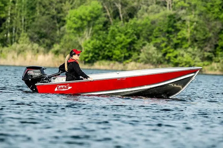 Slide: The Image of Manufacturer Provided Image: 2026 Lund WC-12 boat on a lake, person driving, surrounded by lush greenery. - 9