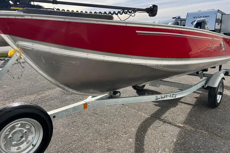 Slide: The Image of 2023 Lund SSV-14 Tiller boat in red on a trailer, clear sky background. - 6