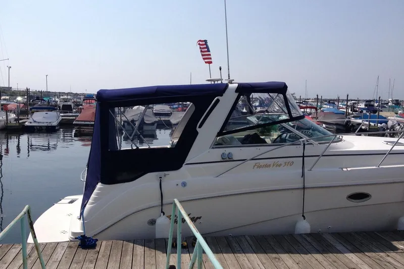 The Image of 2001 Rinker 310 Fiesta Vee boat docked at a marina with American flag. - 1
