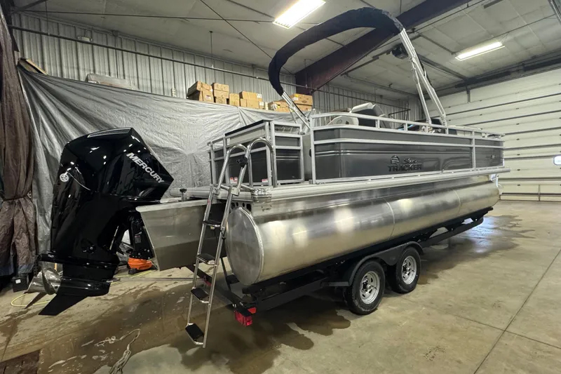 Slide: The Image of 2026 Sun Tracker SportFish 22 XP3 pontoon boat in a garage, featuring a Mercury outboard motor. - 3