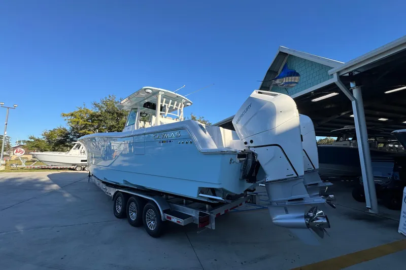 Slide: The Image of 2026 Caymas 34 CT boat with dual Mercury engines on a trailer, parked outdoors. - 11