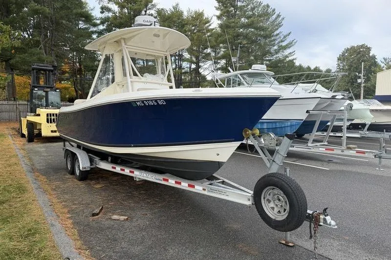 The Image of 2015 Cobia 237CC boat on trailer, parked outdoors near other boats. - 0