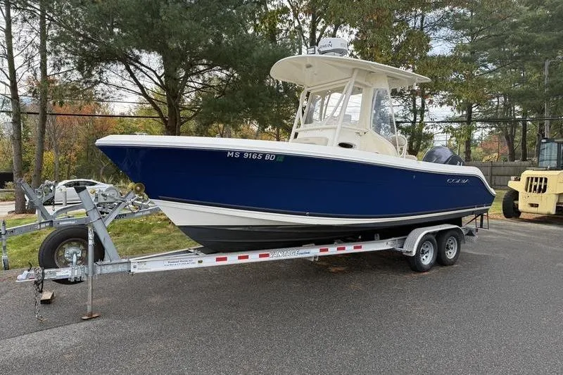 Slide: The Image of 2015 Cobia 237CC boat on trailer, parked outdoors, surrounded by trees. - 7