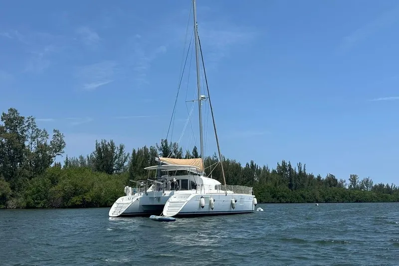 The Image of 2015 Lagoon 380 S2 catamaran anchored on a serene waterway with lush greenery. - 0