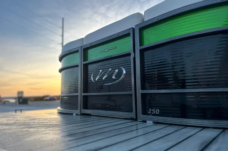 Slide: The Image of 2017 Manitou Xplode 250 pontoon boat at sunset, showcasing sleek design and logo. - 13