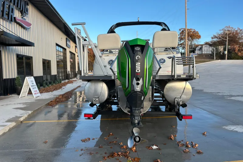 Slide: The Image of 2017 Manitou Xplode 250 pontoon boat with green outboard motor, parked outside a building. - 3