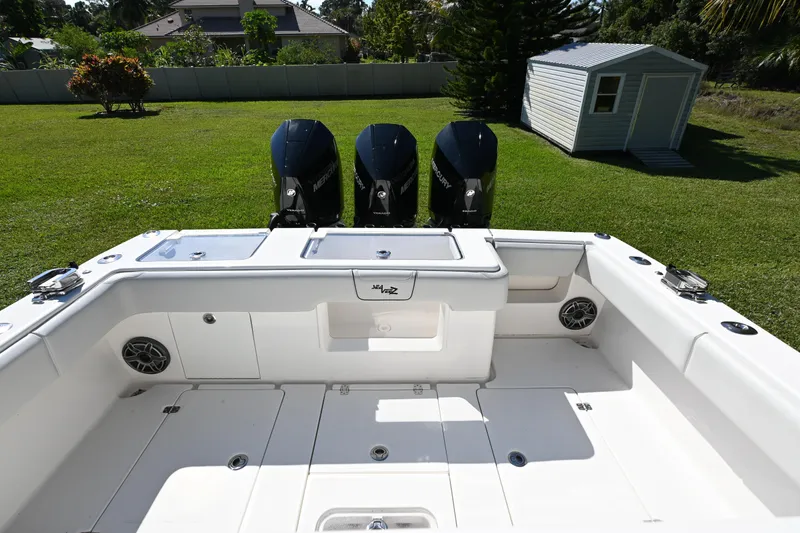 Slide: The Image of 2024 SeaVee 340Z boat with triple Mercury engines, parked on grass near a shed. - 11
