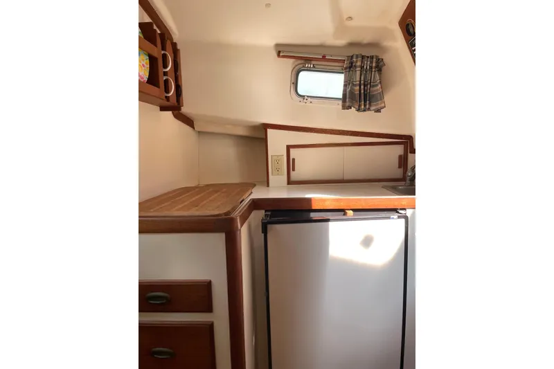 Slide: The Image of 1988 Cape Dory Hardtop interior with kitchenette, featuring wooden cabinets and a small fridge. - 22