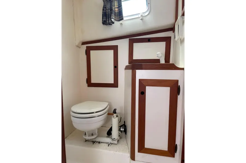 Slide: The Image of 1988 Cape Dory Hardtop boat bathroom with wooden cabinets and a compact toilet. - 27
