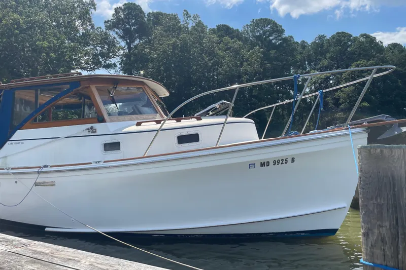 Slide: The Image of 1988 Cape Dory Hardtop boat docked by a wooded shoreline under a clear sky. - 4