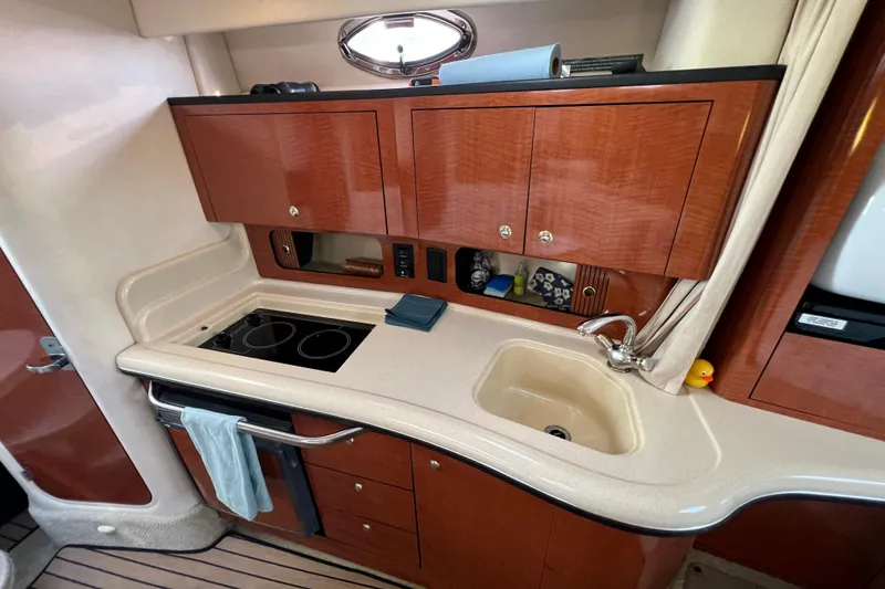 Slide: The Image of 2004 Sea Ray 320 Sundancer kitchen with stove, sink, and wooden cabinets. - 49